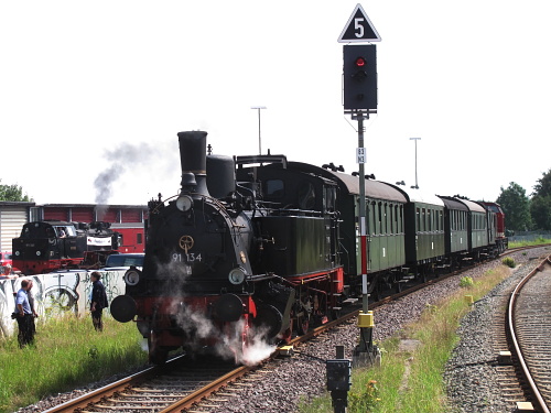 Zwischen Rostock und Bad Doberan pendelten am Samstag und Sonntag die 91 134 und eine V 100 mit ihrem Personenzug. Hier ist der Zug auf dem Bahnhof Bad Doberan zu sehen. Links im Hintergrund ist 99 323 im MOLLI-Bw für Führerstandsmitfahrten unterwegs.